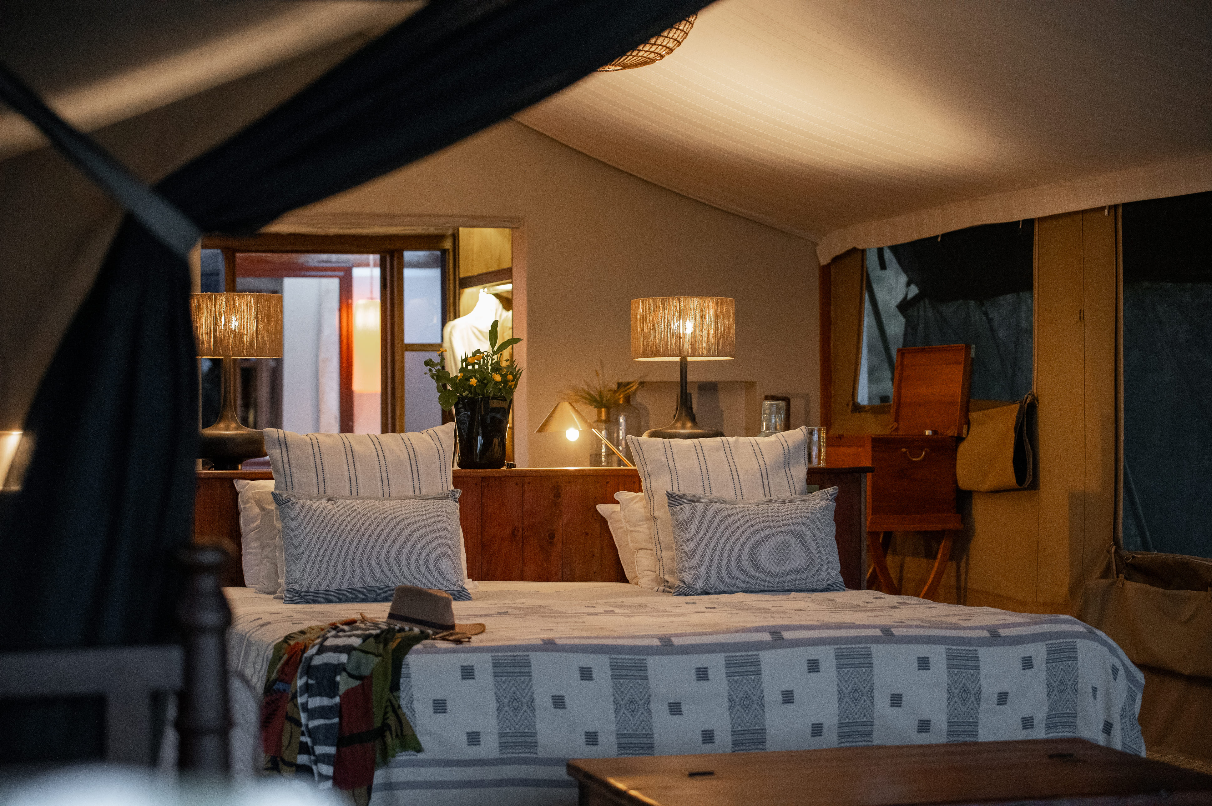 Tented Suite Interior Bedroom: A detailed look inside one of the eight refreshed tented suites at River Camp Mara. The design overhaul has upgraded guest comfort while preserving the camp's historic safari soul, utilizing artisanal fabrics and traditional patterns.